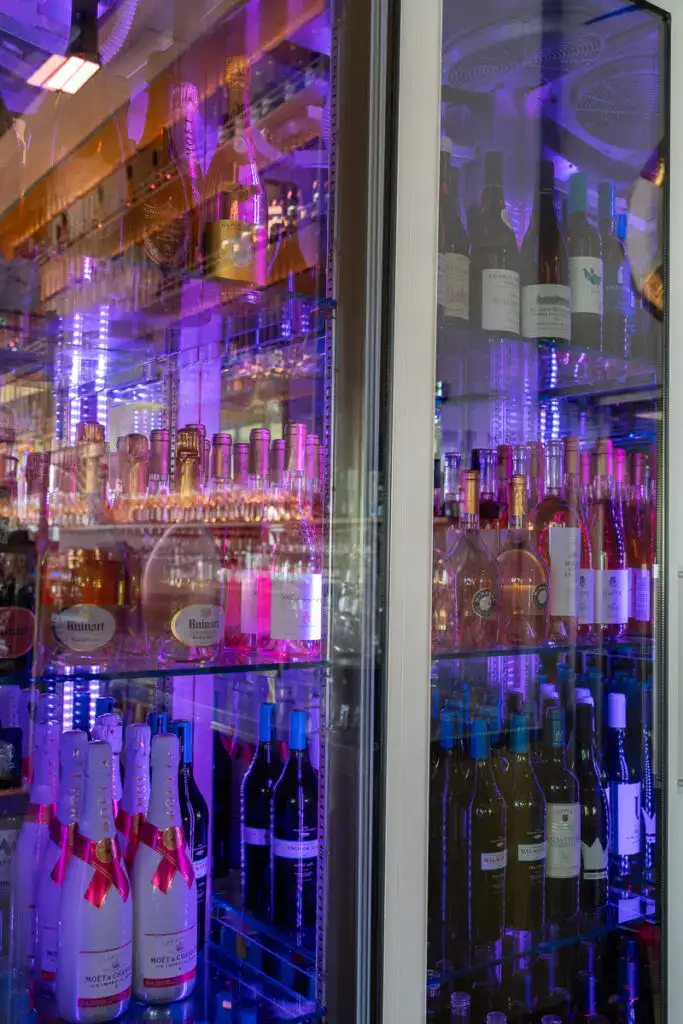 Glasvitrine mit erlesenen Weinen und Champagner Gläsern, beleuchtet mit buntem LED-Licht, für eine moderne Wein- und Spirituosenpräsentation. Perfekt für edle Verkostungen und exklusive Veranstaltungen.