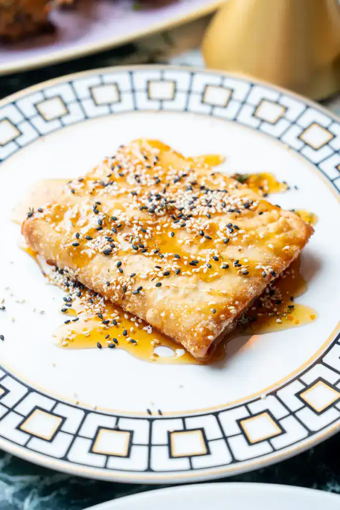 Knuspriges, goldbraunes Fischfilet mit Sesam, Honig und einer leichten Soße auf einem eleganten Kymata Modern Porzellan. Perfekt für moderne Gourmet-Küche und anspruchsvolle Esser.