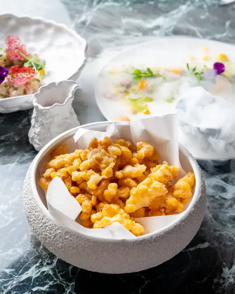 Knusprige, goldene Tempura-Beläge in einer modernen weißen Schale vor einer eleganten, natürlichen Tischdekoration.