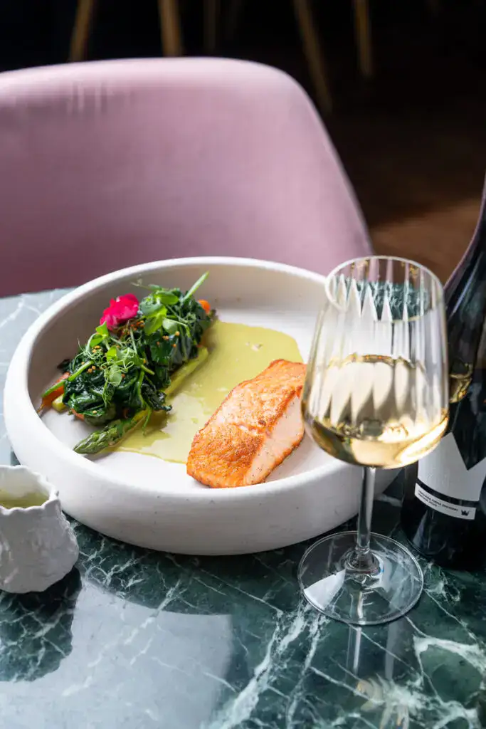 Feines Lachsgericht mit grünem Gemüse und weißem Wein, serviert auf modernem Teller, stilvoll angerichtet. Perfekt für Gourmets und Feinschmecker, ideal für elegante Dinner und besondere Anlässe.