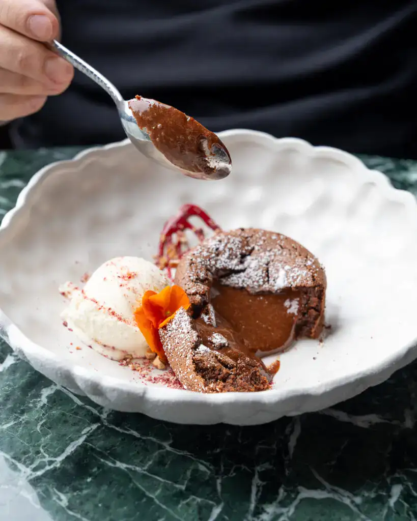 Sauberes, modernes Geschirr auf einem grünen Marmor Tisch zeigt ein schokoladiges Dessert mit Vanilleeis, perfekt für gehobene Gastronomie und Desserts mit innovativem Design.